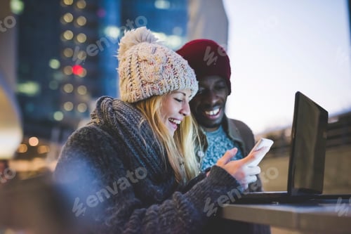 Preview: Couple using smartphone and laptop outdoors at dusk