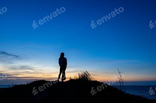 Preview: Silhouette of woman stand at the top of the mountain in the evening
