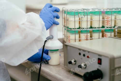 Preview: Gloved lab technician holding donor milk bottle under testing sensor.