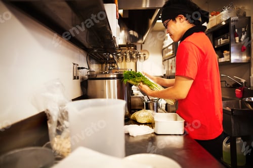 Preview: The ramen noodle shop. A chef working in a kitchen preparing food using a stove and large pans.