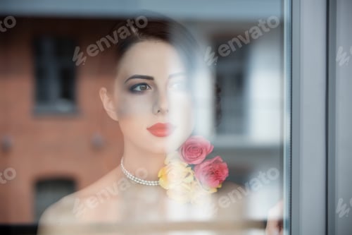 Preview: portrait of beautiful young woman standing near the window and looking at something