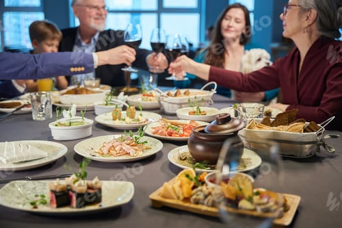 Preview: Delicious dishes on restaurant table people raising wine glasses on background