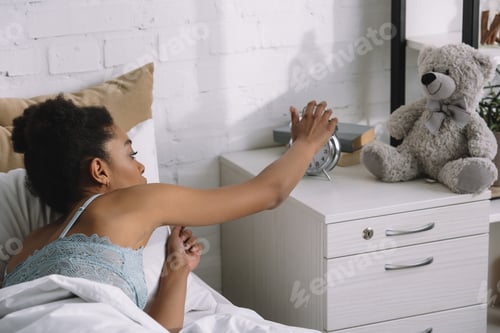 Preview: african american girl waking up and turning off alarm clock in bedroom