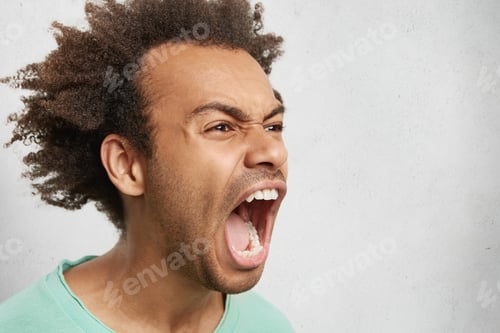 Preview: Half profile of aggressive male with dark curly hair, opens mouth widely, screams in panic, finds ou