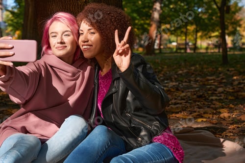 Preview: Two young females taking selfies seated on ground outdoors