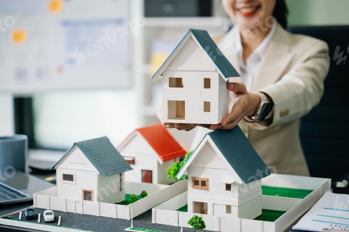 Preview: Young real estate agent worker working with laptop and tablet at table and small house beside it.