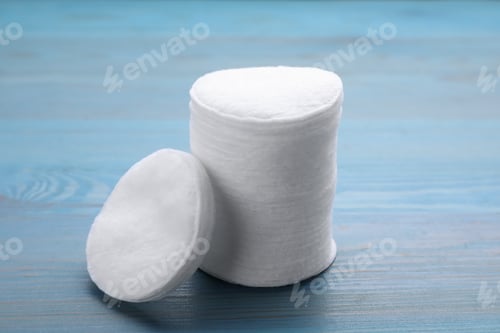 Preview: Stack of clean cotton pads on light blue wooden table, closeup