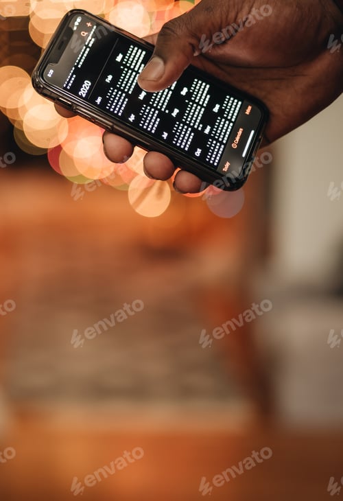 Preview: African American man holding smartphone with calendar visible during holiday time, festive lights