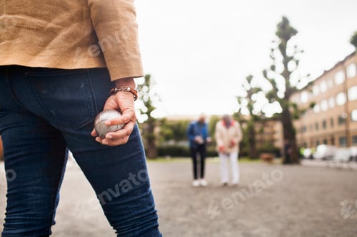 Preview: Closeup of a person ready to bowl in a game of petanque with friends in the background.