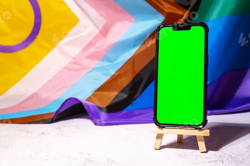 Preview: Mobile phone with chroma key on Rainbow LGBTQIA flag made from silk material background. Happy pride