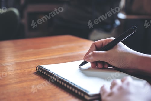 Preview: Closeup image of a hand writing down on a white blank notebook on wooden table