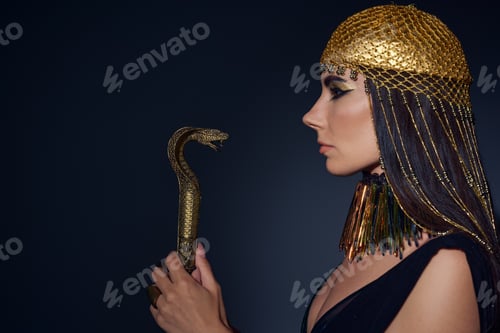 Preview: Side view of woman in egyptian attire holding crook in snake shape on blue background