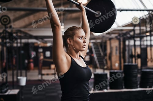 Preview: Focused young woman lifting heavy weights in a gym