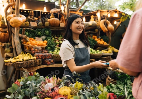 Preview: Woman in an apron working at a farmers market looking at customer.