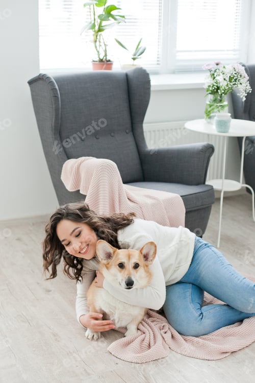Preview: Young woman playing with her welsh corgi dog at cozy home living room, happy family time with pet