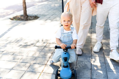 Preview: Happy toddler riding tricycle with parents walking outdoors