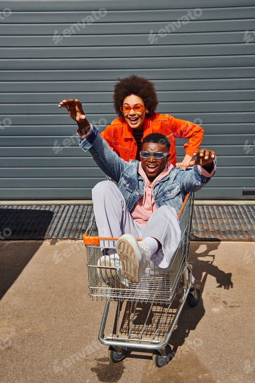 Preview: Cheerful african american woman in bright sunglasses and outfit having fun with best friend sitting
