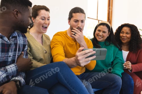 Preview: Happy diverse male and female friends relaxing at home together talking and looking at smartphone
