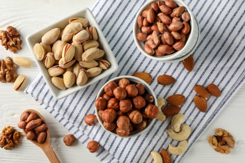 Preview: Bowls with different nuts on white wooden background. Vitamin food
