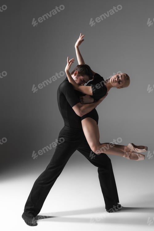 Preview: The Two Young Modern Ballet Dancers In Black Suits Posing Over Gray Studio Background