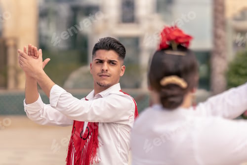 Preview: young male dancer in a red mantillo clapping his hands while dancing flamenco