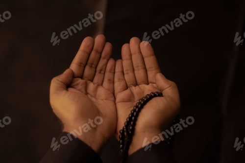 Preview: Muslim man raising his hands to pray with a Tasbeeh on a dark background