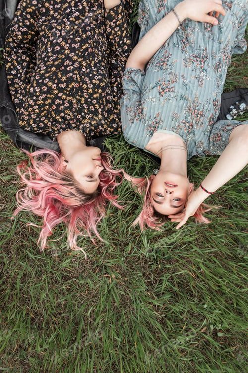 Preview: Trendy girlfriends with pink hair in fashionable summer outfit rests on fresh green grass