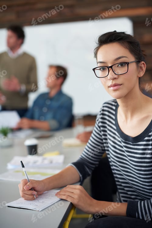 Preview: Portrait of an attractive young woman sitting in an office with colleagues in the background