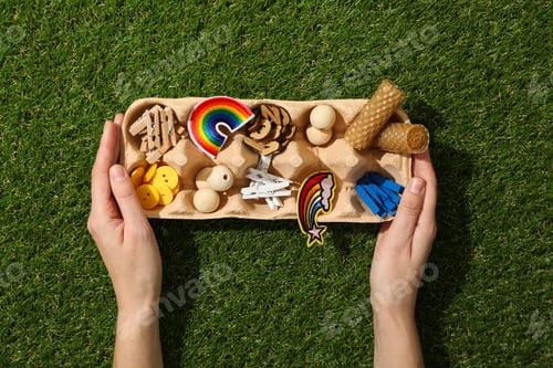 Preview: Art supplies in egg tray in hands on green background, top view