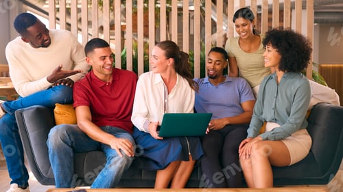 Preview: Multi-Cultural Business Team Sitting On Couch In Modern Open Plan Office Working On Laptop Together