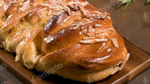 Preview: Golden Braided Sweet Bread with Glazed Topping and Sliced Almonds on a Wooden Board