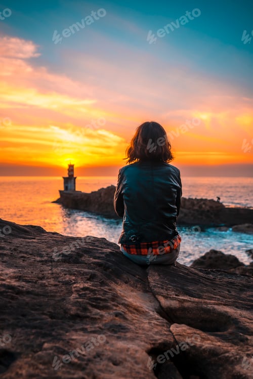 Preview: A young woman sitting on some rocks with a leather jacket in the orange sunset