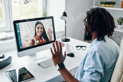 Preview: Happy young African man in shirt talking with smiling woman using computer while sitting indoors