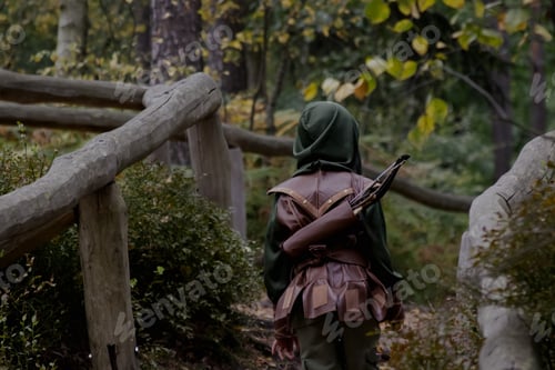 Preview: A back view of a boy in a medieval robber costume walking into the forest