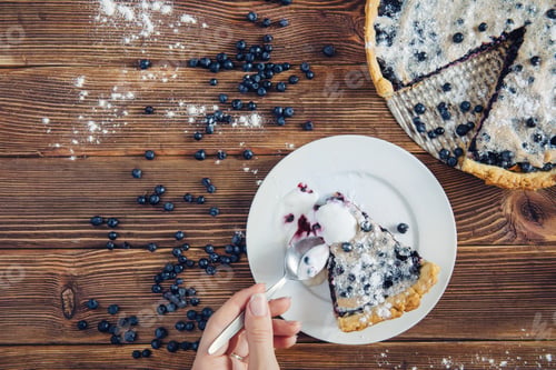 Preview: Eating blueberry pie on dark rustic table served with cream with spoon. Pile of berries near dessert