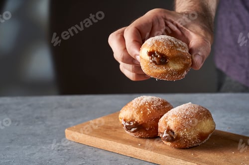 Preview: man's hand serving a Berliner stuffed with dulce de leche