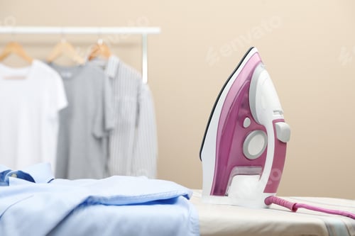 Vista previa: New modern iron and clean shirt on board against beige background, space for text. Laundry day