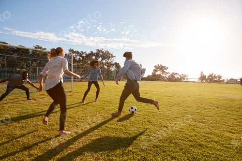 Preview: Four young adults playing football in a park at sunset