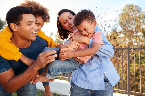 Preview: Young mixed race parents playing outdoors carrying their children in the garden