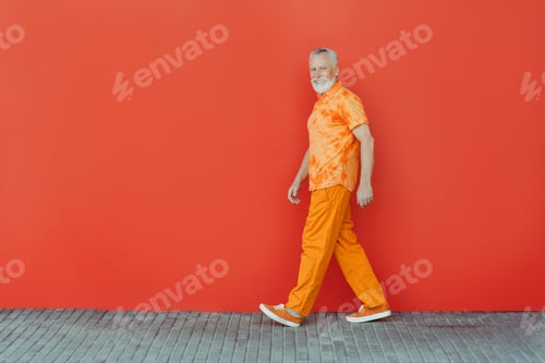 Preview: Smiling senior man, bearded hipster wearing stylish orange clothes walking on the street