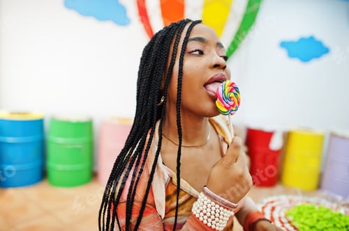 Preview: African american millennial lady at candy shop with lolipops.