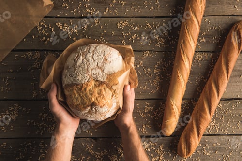 Preview: cropped shot of hands holding loaf of homemade bread and fresh baguettes on table