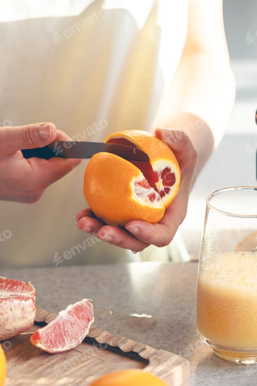 Preview: A woman cuts an orange in the kitchen and makes juice in a juicer.