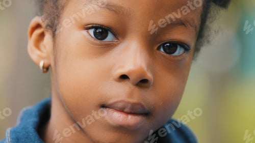 Preview: Close-up little beautiful afro girl in park schoolgirl seriously looking at camera. Portrait of