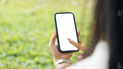 Preview: Female Hand holding a smartphone with empty screen white space mock-up in park outdoor.