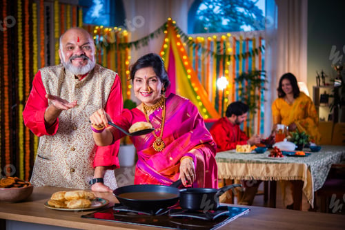 Preview: Indian senior old happy couple cooking food for diwali festival celebration at home