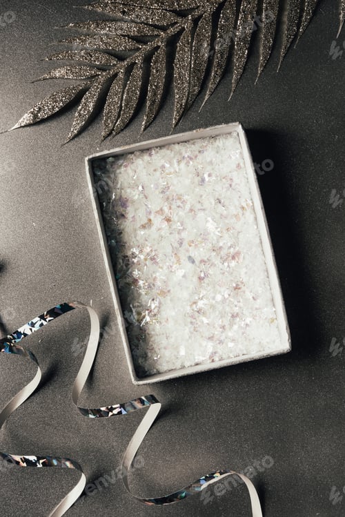Preview: top view of open gift box, silver ribbons and shiny decorative leaves on grey