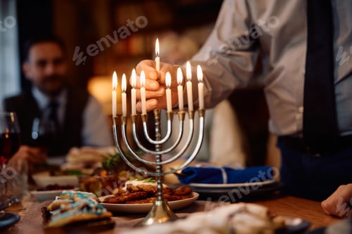 Preview: Close up of senior man lighting candles in menorah while celebrating Hanukkah with his family.