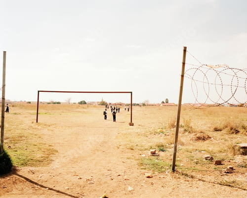 Preview: View across an arid common, barbed wire on a pole, group of children walking in the distance.