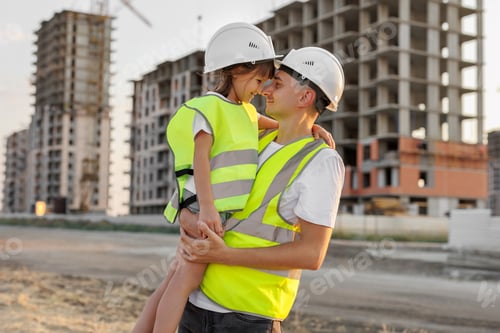 Preview: Portrait of a father and daughter in protective helmets on the background of a construction site.
